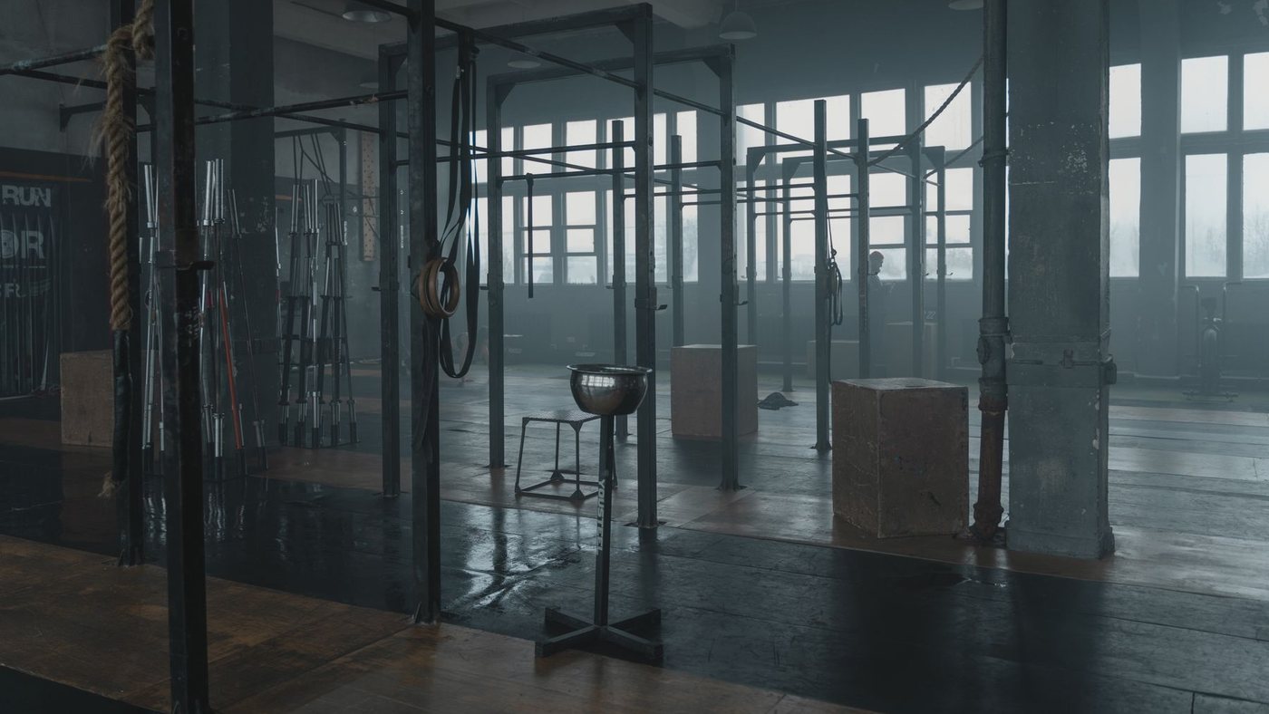 Sala de treino industrial vazia, com equipamento parado e neblina ao fundo